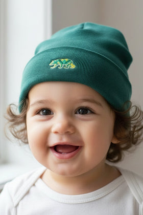 Child wearing a green dapper bear beanie with a logo, standing indoors near a window.