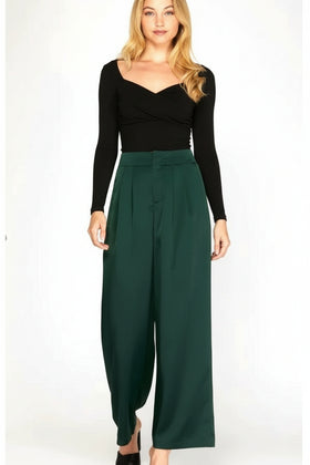 Woman wearing a black long-sleeve top and green wide-leg pants on a white background