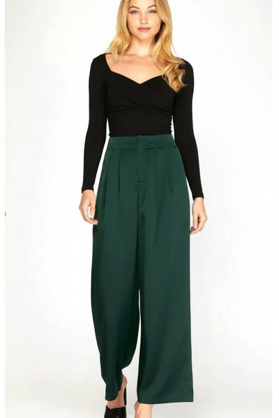 Woman wearing a black long-sleeve top and green wide-leg pants on a white background