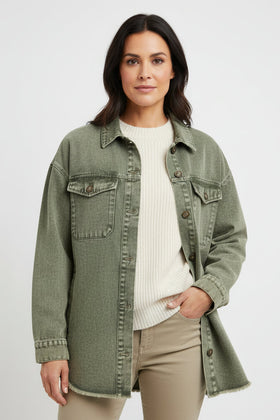 Woman wearing a green denim jacket over a white shirt and beige pants on a light gray background