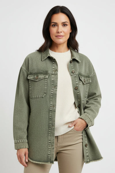 Woman wearing a green denim jacket over a white shirt and beige pants on a light gray background